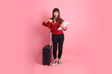 Kırmızı tişörtlü Asyalı kız öğrenci ya da günlük giysiler içinde okul çantası ve pembe arka planda izole edilmiş bir işaret işareti içeren bavul taşıyorlar. Gen Z