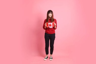 Kırmızı tişörtlü ya da sıradan giysili Asyalı kız öğrenci pembe arka planda izole edilmiş Kanada ya da Kanada bayrağı taşıyan bir jestle okul çantası taşıyor. Gen Z