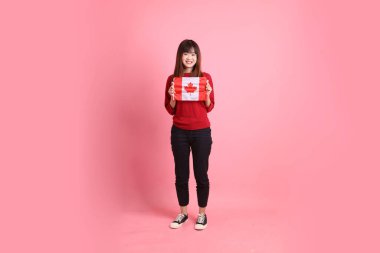 Kırmızı tişörtlü ya da sıradan giysili Asyalı kız öğrenci pembe arka planda izole edilmiş Kanada ya da Kanada bayrağı taşıyan bir jestle okul çantası taşıyor. Gen Z