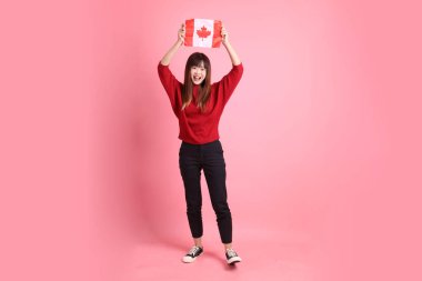 Kırmızı tişörtlü ya da sıradan giysili Asyalı kız öğrenci pembe arka planda izole edilmiş Kanada ya da Kanada bayrağı taşıyan bir jestle okul çantası taşıyor. Gen Z