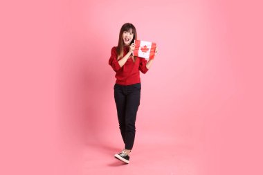 Kırmızı tişörtlü ya da sıradan giysili Asyalı kız öğrenci pembe arka planda izole edilmiş Kanada ya da Kanada bayrağı taşıyan bir jestle okul çantası taşıyor. Gen Z