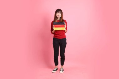 Kırmızı tişörtlü ya da sıradan giysili Asyalı kız öğrenci, pembe arka planda izole edilmiş Alman bayrağı ya da Alman bayrağı taşıyan okul çantası taşıyor. Gen Z