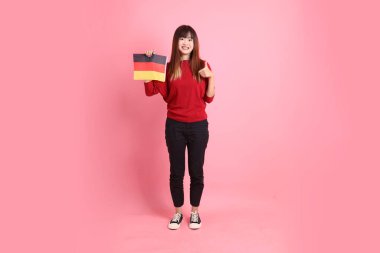 Kırmızı tişörtlü ya da sıradan giysili Asyalı kız öğrenci, pembe arka planda izole edilmiş Alman bayrağı ya da Alman bayrağı taşıyan okul çantası taşıyor. Gen Z
