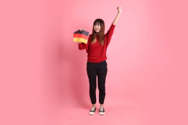 Kırmızı tişörtlü ya da sıradan giysili Asyalı kız öğrenci, pembe arka planda izole edilmiş Alman bayrağı ya da Alman bayrağı taşıyan okul çantası taşıyor. Gen Z