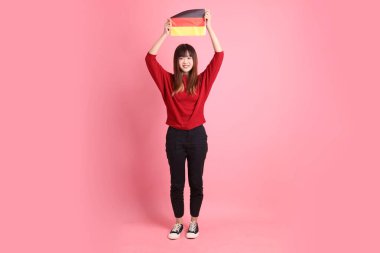 Kırmızı tişörtlü ya da sıradan giysili Asyalı kız öğrenci, pembe arka planda izole edilmiş Alman bayrağı ya da Alman bayrağı taşıyan okul çantası taşıyor. Gen Z