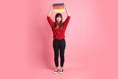 Kırmızı tişörtlü ya da sıradan giysili Asyalı kız öğrenci, pembe arka planda izole edilmiş Alman bayrağı ya da Alman bayrağı taşıyan okul çantası taşıyor. Gen Z