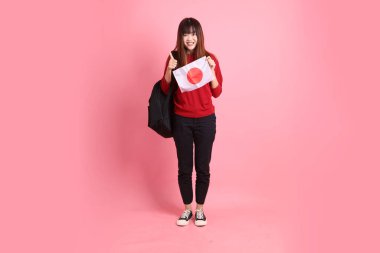 Kırmızı tişörtlü ya da sıradan giysili Asyalı bir kız öğrenci pembe arka planda Japon ya da Japon bayrağı taşıyan bir jestle okul çantası taşıyor. Gen Z