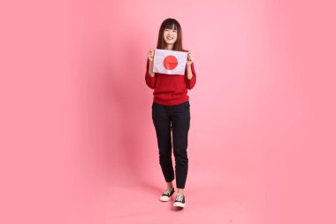Kırmızı tişörtlü ya da sıradan giysili Asyalı bir kız öğrenci pembe arka planda Japon ya da Japon bayrağı taşıyan bir jestle okul çantası taşıyor. Gen Z