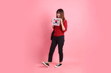 Kırmızı tişörtlü ya da sıradan giysili Asyalı kız öğrenci pembe arka planda Kore ya da Kore bayrağı saklama hareketi içeren okul çantası taşıyor. Gen Z