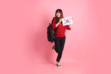 Kırmızı tişörtlü ya da sıradan giysili Asyalı kız öğrenci pembe arka planda Kore ya da Kore bayrağı saklama hareketi içeren okul çantası taşıyor. Gen Z