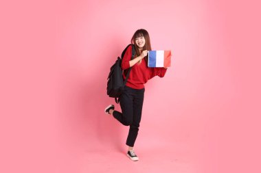 Kırmızı tişörtlü ya da sıradan giysili Asyalı kız öğrenci pembe arka planda Fransız ya da Fransız bayrağı taşıyan okul çantası taşıyor. Gen Z