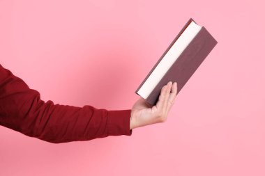 Mutlu Çin Yeni Yılı, resmi ve sıradan kırmızı tişörtlü Asyalı son sınıf öğrencisi pembe arka planda izole edilmiş bir kitabı tutuyor..