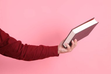 Mutlu Çin Yeni Yılı, resmi ve sıradan kırmızı tişörtlü Asyalı son sınıf öğrencisi pembe arka planda izole edilmiş bir kitabı tutuyor..