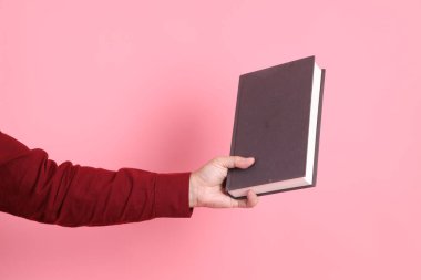 Mutlu Çin Yeni Yılı, resmi ve sıradan kırmızı tişörtlü Asyalı son sınıf öğrencisi pembe arka planda izole edilmiş bir kitabı tutuyor..