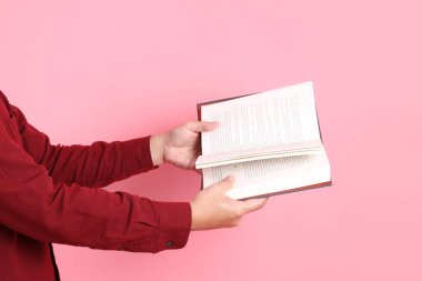 Mutlu Çin Yeni Yılı, resmi ve sıradan kırmızı tişörtlü Asyalı son sınıf öğrencisi pembe arka planda izole edilmiş bir kitabı tutuyor..