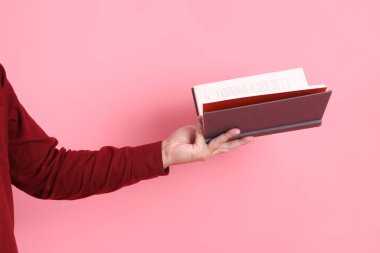 Mutlu Çin Yeni Yılı, resmi ve sıradan kırmızı tişörtlü Asyalı son sınıf öğrencisi pembe arka planda izole edilmiş bir kitabı tutuyor..