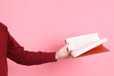 Mutlu Çin Yeni Yılı, resmi ve sıradan kırmızı tişörtlü Asyalı son sınıf öğrencisi pembe arka planda izole edilmiş bir kitabı tutuyor..