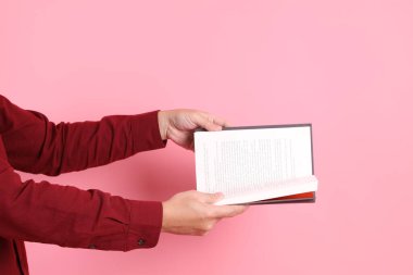 Mutlu Çin Yeni Yılı, resmi ve sıradan kırmızı tişörtlü Asyalı son sınıf öğrencisi pembe arka planda izole edilmiş bir kitabı tutuyor..