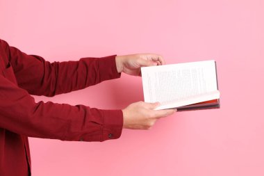 Mutlu Çin Yeni Yılı, resmi ve sıradan kırmızı tişörtlü Asyalı son sınıf öğrencisi pembe arka planda izole edilmiş bir kitabı tutuyor..