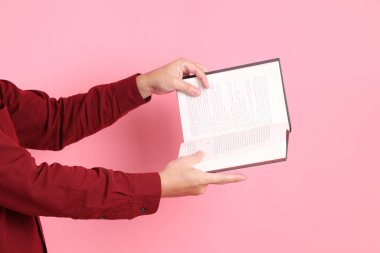 Mutlu Çin Yeni Yılı, resmi ve sıradan kırmızı tişörtlü Asyalı son sınıf öğrencisi pembe arka planda izole edilmiş bir kitabı tutuyor..