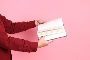 Mutlu Çin Yeni Yılı, resmi ve sıradan kırmızı tişörtlü Asyalı son sınıf öğrencisi pembe arka planda izole edilmiş bir kitabı tutuyor..