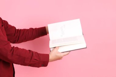 Mutlu Çin Yeni Yılı, resmi ve sıradan kırmızı tişörtlü Asyalı son sınıf öğrencisi pembe arka planda izole edilmiş bir kitabı tutuyor..