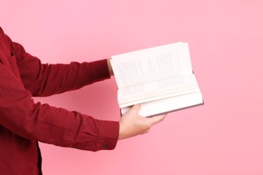 Mutlu Çin Yeni Yılı, resmi ve sıradan kırmızı tişörtlü Asyalı son sınıf öğrencisi pembe arka planda izole edilmiş bir kitabı tutuyor..