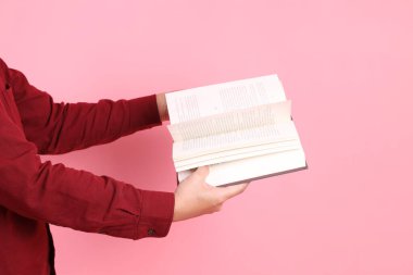 Mutlu Çin Yeni Yılı, resmi ve sıradan kırmızı tişörtlü Asyalı son sınıf öğrencisi pembe arka planda izole edilmiş bir kitabı tutuyor..