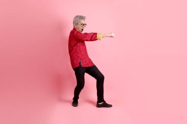 Yeni Çin yılın kutlu olsun. Asya 'nın son sınıf öğrencisi, geleneksel kırmızı Cheongsam Qipao ya da Changshan elbisesi giyiyor. Pembe arka planda izole edilmiş bir dövüş jesti..