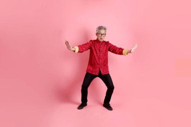 Yeni Çin yılın kutlu olsun. Asya 'nın son sınıf öğrencisi, geleneksel kırmızı Cheongsam Qipao ya da Changshan elbisesi giyiyor ve pembe arka planda izole edilmiş Tai Chi hareketi yapıyor..