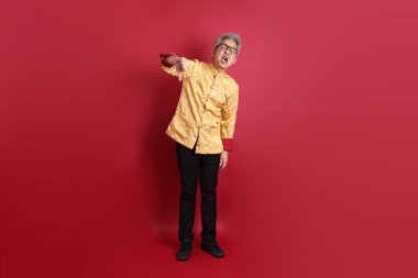 Yeni Çin yılın kutlu olsun. Asya 'lı son sınıf öğrencisi altın rengi Cheongsam Qipao ya da Changshan elbisesi giyiyor. Kırmızı arka planda izole edilmiş baş parmak işareti var..