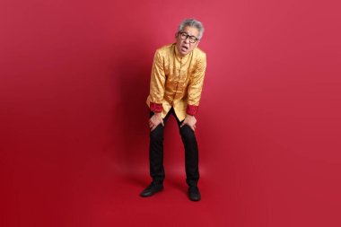 Yeni Çin yılın kutlu olsun. Asya 'nın son sınıf öğrencisi altın rengi Cheongsam Qipao ya da Changshan elbisesi giyiyor. Kırmızı arka planda soyutlanmış, bitkin, tembel davranışlar sergiliyor..