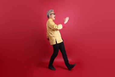 Yeni Çin yılın kutlu olsun. Asya 'nın son sınıf öğrencisi altın rengi Cheongsam Qipao ya da Changshan elbisesi giyiyor. Kırmızı arka planda izole bir şekilde yürüyor..