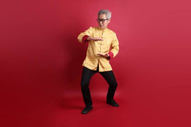 Yeni Çin yılın kutlu olsun. Asya 'nın son sınıf öğrencisi altın rengi Cheongsam Qipao ya da Changshan elbisesi giyiyor ve kırmızı arka planda izole edilmiş Tai Chi hareketi yapıyor..