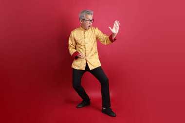 Yeni Çin yılın kutlu olsun. Asya 'nın son sınıf öğrencisi altın rengi Cheongsam Qipao ya da Changshan elbisesi giyiyor ve kırmızı arka planda izole edilmiş Tai Chi hareketi yapıyor..