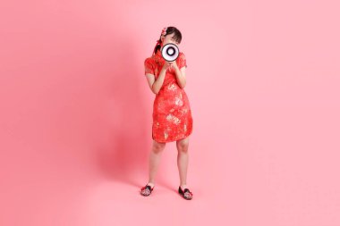 Yeni Çin yılın kutlu olsun. Asyalı Çinli bir kadın geleneksel kırmızı Cheongsam Qipao giyiyor ve bağrışmalar yapıyor. Elinde pembe arka planda izole edilmiş megafon taşıyor. Gen Z