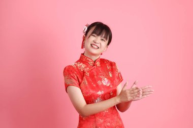Yeni Çin yılın kutlu olsun. Asyalı Çinli kadın geleneksel kırmızı Cheongsam Qipao giyiyor ve pembe arka planda el çırpma hareketi yapıyor. Gen Z