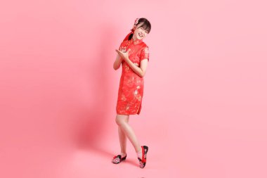 Yeni Çin yılın kutlu olsun. Asyalı Çinli kadın geleneksel kırmızı Cheongsam Qipao giyiyor ve pembe arka planda el çırpma hareketi yapıyor. Gen Z