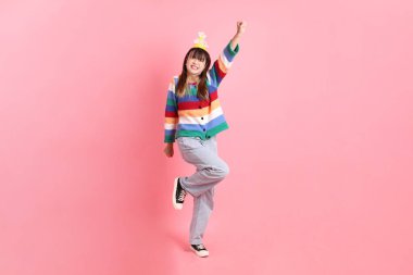 Mutlu yıllar, renkli gökkuşağı kış elbiseli Asyalı kadın, sıradan görünüşlü, evet jestli doğum günü şapkası, heyecanlı, pembe arka planda izole edilmiş kutlamayı kutlayan. Gen Z, 