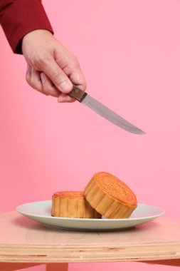 Geleneksel Çin tatlısını kesmek için el ele tutuşan bıçak ya da pembe arka planda izole edilmiş Çin pastası. Çin Geleneksel Sonbahar Festivali, Ay Festivali.