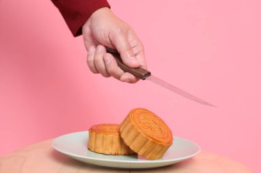 Geleneksel Çin tatlısını kesmek için el ele tutuşan bıçak ya da pembe arka planda izole edilmiş Çin pastası. Çin Geleneksel Sonbahar Festivali, Ay Festivali.