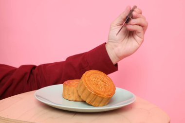 Geleneksel Çin tatlısını kesmek için el ele tutuşan bıçak ya da pembe arka planda izole edilmiş Çin pastası. Çin Geleneksel Sonbahar Festivali, Ay Festivali.