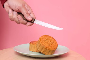 Geleneksel Çin tatlısını kesmek için el ele tutuşan bıçak ya da pembe arka planda izole edilmiş Çin pastası. Çin Geleneksel Sonbahar Festivali, Ay Festivali.