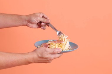 Turuncu arka planda izole edilmiş yeşil bir tabakta, çatallı kremalı spagetti yiyen. İtalyan yemeği, İtalyan mutfağı, erişte..