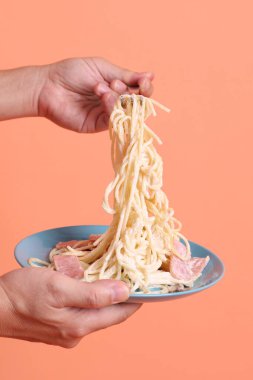 Turuncu arka planda izole edilmiş yeşil bir tabakta, çatallı kremalı spagetti yiyen. İtalyan yemeği, İtalyan mutfağı, erişte..