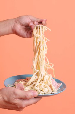 Turuncu arka planda izole edilmiş yeşil bir tabakta, çatallı kremalı spagetti yiyen. İtalyan yemeği, İtalyan mutfağı, erişte..