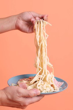 Turuncu arka planda izole edilmiş yeşil bir tabakta, çatallı kremalı spagetti yiyen. İtalyan yemeği, İtalyan mutfağı, erişte..