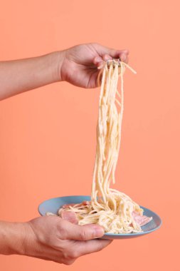 Turuncu arka planda izole edilmiş yeşil bir tabakta, çatallı kremalı spagetti yiyen. İtalyan yemeği, İtalyan mutfağı, erişte..