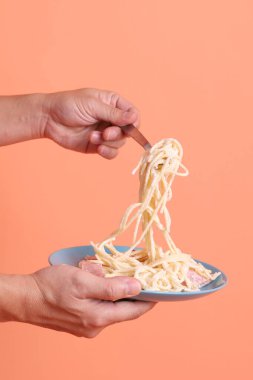 Turuncu arka planda izole edilmiş yeşil bir tabakta, çatallı kremalı spagetti yiyen. İtalyan yemeği, İtalyan mutfağı, erişte..