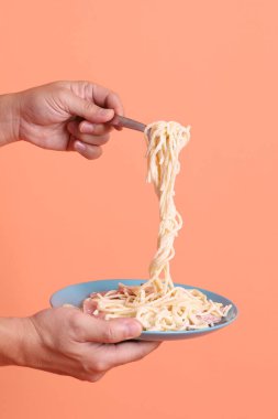 Turuncu arka planda izole edilmiş yeşil bir tabakta, çatallı kremalı spagetti yiyen. İtalyan yemeği, İtalyan mutfağı, erişte..